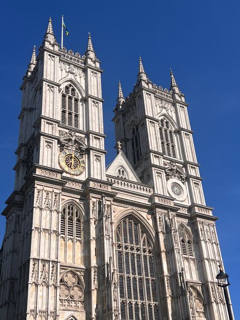 A red double-decker bus with route number 453 and destination Marylebone is parked on a wet city street in Westminster, near historic Gothic-style buildings and the Palace of Westminster with its tall